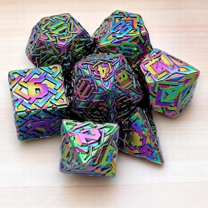 Könnte beinhalten: Eine Sammlung schillernder, vielseitiger Würfel. Die Würfel haben verschiedene geometrische Formen, mit Zahlen auf jeder Seite. Die Farben wechseln von Lila zu Grün und Gold und erzeugen einen Regenbogeneffekt. Die Würfel liegen auf einer hellen Holzoberfläche.