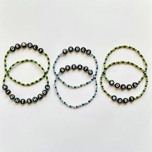 May include: Three beaded bracelets with black letter beads spelling "DEADLY NIGHTSHADE", "FROGS BREATH", and "WORMS WORT". The bracelets have green, yellow, and purple beads.