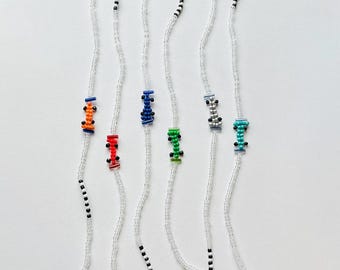 May include: Six beaded bracelets featuring clear seed beads and small, colourful race car motifs made from beads. Each bracelet includes a metal lobster clasp and a short segment of black and white beads near the closure. The car designs are orange, red, blue, green, silver, and teal.
