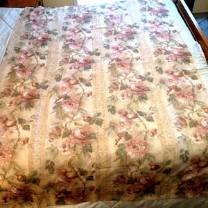 May include: A floral patterned bedspread featuring a repeating design of pink roses and green leaves on a cream-colored background. The bedspread has vertical stripes and is made of a soft, possibly cotton, material.