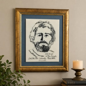 May include: A framed wall art piece featuring a black ink line drawing of a bearded face on a white background. The text reads: Seek the Lord and His Strength; Seek His Face Continually. Psalm 105:4. The frame is gold with a dark blue mat border.