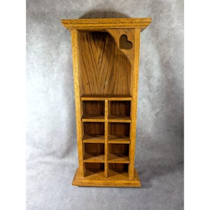 May include: A tall, light brown wooden wall shelf featuring a vertical grain pattern. The unit has a flat top, a central divider creating two columns, and four horizontal shelves on each side. A cutout heart shape is visible in the upper corner.