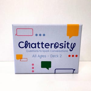 May include: A light blue box with the word "Chatterosity" in dark blue, with the tagline "Questions to Spark Conversations." The box also includes the text "All Ages - Deck 2" and colorful speech bubble graphics.