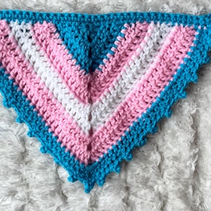 May include: A crocheted triangle with a scalloped edge in blue, pink, and white colors. The colors are arranged in a pattern that resembles the transgender pride flag.