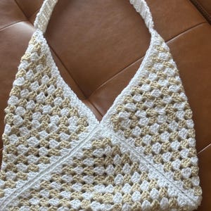 May include: A white and beige crocheted tote bag with a triangular shape and a long strap.