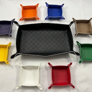 May include: A collection of leather valet trays in various colors, including orange, blue, yellow, white, red, green, and tan. The trays have a diamond-stitched pattern and are designed with folded corners.