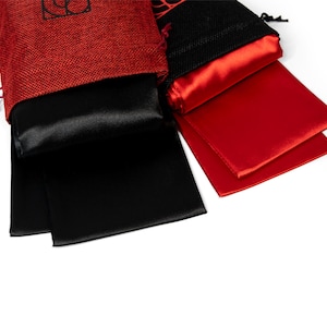 May include: Two small drawstring bags, one red and one black, each containing a satin item. The red bag is made of a textured fabric, while the black bag is a mesh. The satin items are black and red, respectively.