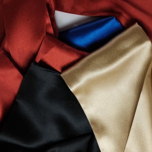 May include: A selection of folded satin fabric in shades of red, blue, black, and gold. The fabric has a smooth, glossy finish. The image shows a close-up of the fabric.