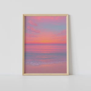 Könnte beinhalten: Ein vertikaler, rechteckiger Wandkunstdruck in einem hellen Holzrahmen, der einen Sonnenuntergang über dem Ozean zeigt. Der Himmel zeigt Farbverläufe in Rosa, Orange und sanftem Blau. Das ruhige Wasser spiegelt die Farben wider und trifft auf einen Sandstrand.