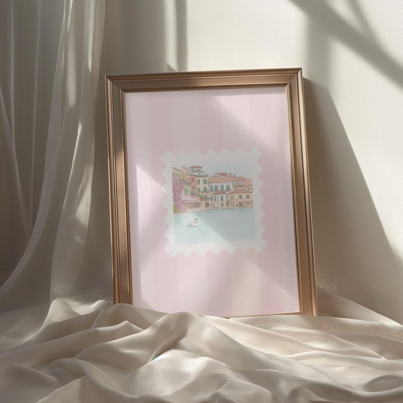 Pu&ograve; includere: Una stampa incorniciata con un'illustrazione ad acquerello di un paesaggio acquatico europeo. L'opera d'arte, su uno sfondo a righe rosa, raffigura edifici con tetti rossi e un cigno sull'acqua. La cornice &egrave; dorata.