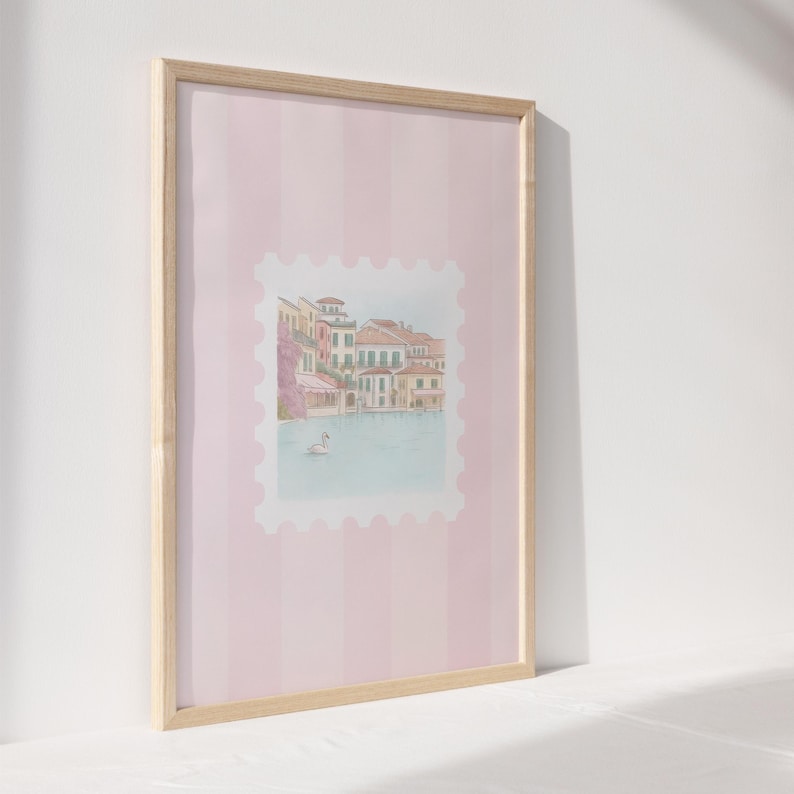 Pu&ograve; includere: Stampa artistica incorniciata con un'illustrazione ad acquerello di un paesaggio europeo sul lungomare. L'opera d'arte &egrave; ambientata su uno sfondo a righe rosa e incorniciata in legno naturale. Un cigno galleggia sull'acqua.
