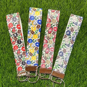 May include: Four keychains with floral and football patterns. Each keychain features a different design: red flowers, yellow flowers, red flowers, and blue flowers. The keychains have brown leather accents and silver key rings.