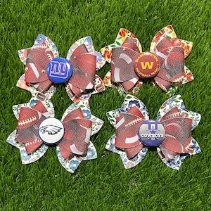 May include: Six handmade hair bows with football and team logo designs. Each bow features a football print and a team button. The teams represented are the Giants, Commanders, Eagles, and Cowboys. The bows are set on a green grass background.