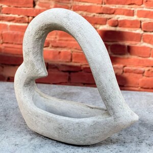 May include: A gray concrete heart-shaped planter with a smooth, textured surface. The planter is designed to hold small plants or flowers.