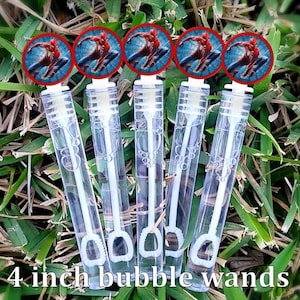May include: Five clear plastic bubble wands, each with a white handle and a 4-inch length. Each wand is topped with a red-rimmed circular image of Spider-Man. The wands are arranged on a bed of green grass.
