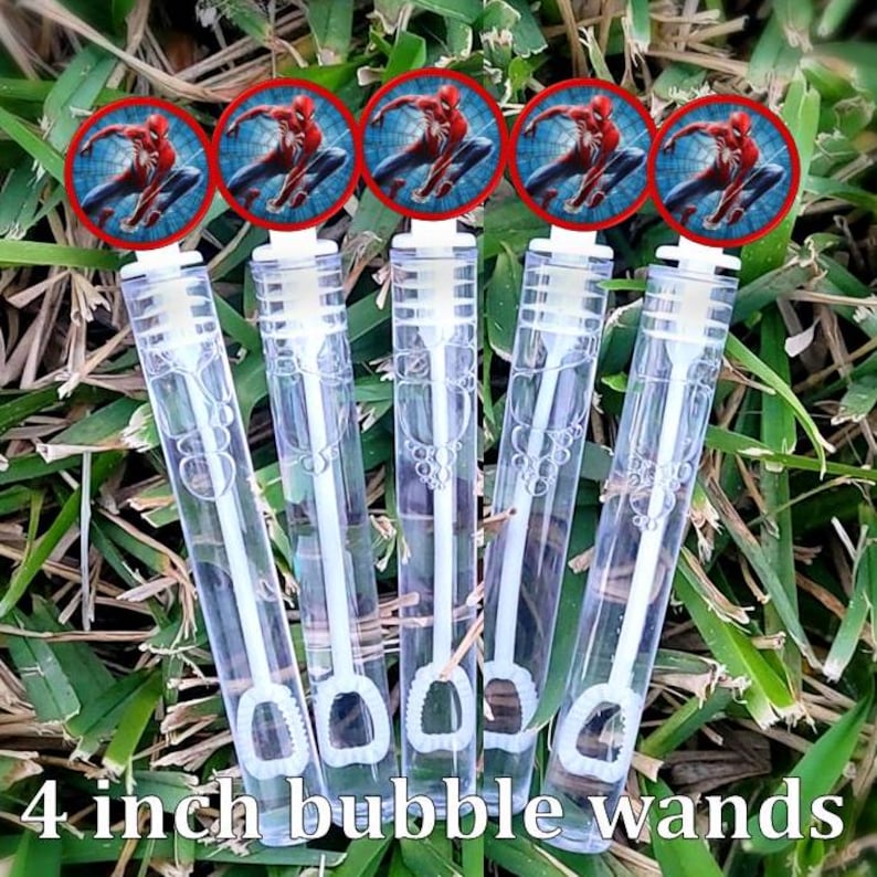 May include: Five clear plastic bubble wands, each with a white handle and a 4-inch length. Each wand is topped with a red-rimmed circular image of Spider-Man. The wands are arranged on a bed of green grass.