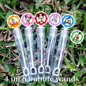 May include: Five clear plastic bubble wands with character toppers featuring Goofy, Minnie Mouse, Mickey Mouse, Daisy Duck, and Donald Duck. The bubble wands are 4 inches long. The wands are arranged on a bed of green grass.