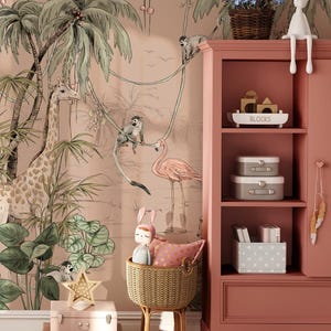 Puede incluir: Una habitación de bebé rosa y marrón con un mural de jungla que presenta una jirafa, monos y un flamenco. Una estantería de madera con una etiqueta blanca que dice "BLOCKS" está en el lado derecho de la imagen. La estantería tiene un juguete de conejo blanco en la parte superior y una variedad de cajas de almacenamiento y libros en los estantes. Una cesta de mimbre con un juguete de conejo de peluche y una almohada rosa está en la esquina inferior izquierda de la imagen.