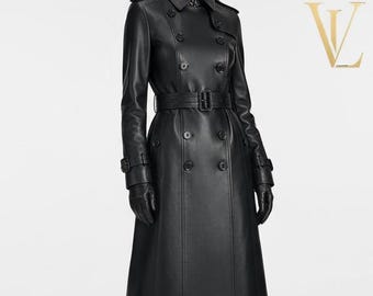 Op de afbeelding: Een zwarte leren double-breasted trenchcoat met een reverskraag, lange mouwen met gespmanchetten, een bijpassende ceintuur met gesp in de taille en een zoom tot halverwege de kuit. De jas wordt gedragen met zwarte leren handschoenen en laarzen.