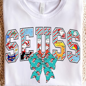 May include: White t-shirt with a red and white striped design featuring the word "SEUSS" in large letters. The letters are filled with images of characters from Dr. Seuss books. A green and blue bow is below the word.
