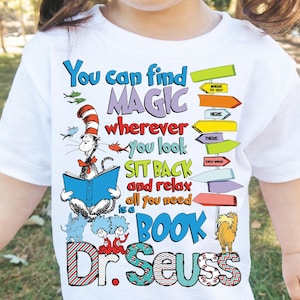 Op de afbeelding: Wit T-shirt met een kleurrijke afbeelding van de Kat in de Hoed die een boek leest, samen met andere Dr. Seuss-personages. De tekst luidt "You can find MAGIC wherever you look SIT BACK and relax all you need is a BOOK Dr. Seuss".