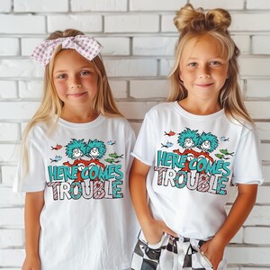 May include: Two children wearing white t-shirts with a graphic of the Cat in the Hat characters and the text "Here Comes Trouble".
