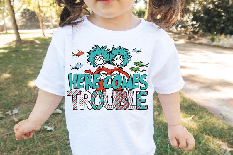 May include: White t-shirt with a graphic of two blue and green characters with red shirts and the text "Here Comes Trouble" in blue and green letters with red and white stripes.