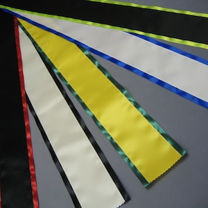 May include: Five different colored sashes with contrasting trim. The sashes are made of satin and have a smooth, silky texture. The colors are black, white, yellow, blue, and green.