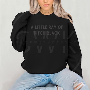 May include: Black sweatshirt with the text "A little ray of pitch black" and "Shop with Kayyyy" printed on the front.