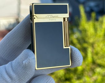 May include: A gold and black S.T. Dupont lighter with the words "S.T. Dupont" and "Paris" engraved on the front.