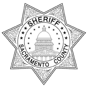 May include: Black and white illustration of a sheriff's badge with a star shape and the words "SHERIFF SACRAMENTO COUNTY" around the perimeter. The badge features a stylized image of the California State Capitol building.