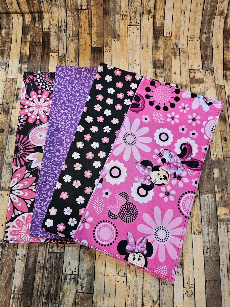Op de afbeelding: Vier vierkante stukken stof met verschillende patronen. De eerste vierkant heeft een roze en zwart bloemenpatroon. De tweede vierkant heeft een paars bloemenpatroon. De derde vierkant heeft een zwart-wit stippenpatroon met kleine roze bloemen. De vierde vierkant heeft een roze achtergrond met een wit en roze bloemenpatroon en een cartoon afbeelding van Minnie Mouse.