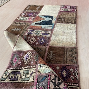 Könnte beinhalten: Ein rechteckiger Patchwork-Teppich mit einer Vielzahl von Mustern und Farben. Der Teppich zeigt Quadrate in Braun-, Beige- und Lilatönen mit geometrischen und floralen Designs. Der Teppich ist teilweise gefaltet und zeigt seine Unterseite.