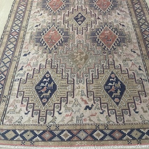 May include: An intricately patterned rug with a beige background and geometric designs in navy, rust, and brown. The rug features repeating diamond and rectangular shapes with animal and bird motifs, framed by a border.