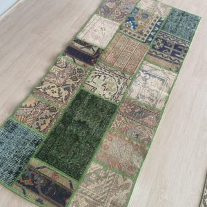 Könnte beinhalten: Ein rechteckiger Patchwork-Teppich mit grünem Rand. Der Teppich besteht aus verschiedenen rechteckigen Flicken in Grün-, Beige-, Braun- und Blautönen. Die Flicken weisen komplizierte Muster und Designs auf und schaffen eine Vintage-Ästhetik.