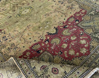 Könnte beinhalten: Ein antiker Teppich mit einem abgenutzten, Vintage-Aussehen. Der Teppich hat ein zentrales Feld in Olivgrün und Beige, mit einem roten und olivgrünen Rand. Das Design umfasst florale und geometrische Muster.