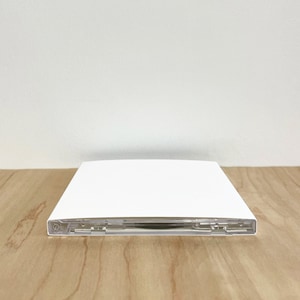 May include: A white CD case with a clear plastic tray. The case is closed and sitting on a wooden surface.