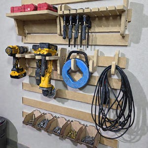 Könnte beinhalten: Ein wandmontierter Werkzeugorganizer aus Holz mit verschiedenen Werkzeugen und Zubehör. Enthält ein Regal mit roten Werkzeugkästen, Bohrmaschine, Schleifer, Klemmen, eine blaue Kabeltrommel und Fächer für Schrauben und Nägel. Die Werkzeuge sind gelb und schwarz.