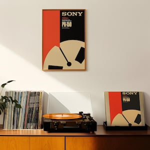 Op de afbeelding: Een modern houten kastje in mid-century stijl met een platenspeler, een stapel vinylplaten en twee ingelijste posters met de tekst "SONY" en "PS-150" in rood en zwart.