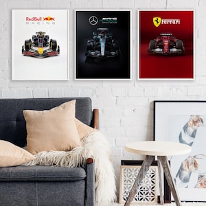 May include: Three framed Formula 1 racing car posters. The posters feature Red Bull Racing, Mercedes-AMG Petronas, and Ferrari cars. The Red Bull poster is on a white background, the Mercedes poster is on a black background, and the Ferrari poster is on a red background.