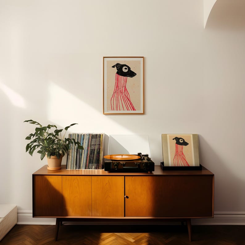 Puede incluir: Un armario de madera de estilo moderno de mediados de siglo con un tocadiscos, discos de vinilo y dos impresiones enmarcadas de un perro negro con un su&eacute;ter rojo.