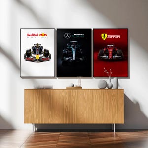 May include: Three framed Formula 1 racing car posters. The first features a Red Bull car, the second a Mercedes, and the third a Ferrari. The posters are displayed above a wooden cabinet. The Red Bull poster has the text "Red Bull Racing".