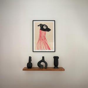 Puede incluir: Una impresi&oacute;n enmarcada de una ilustraci&oacute;n en blanco y negro de un perro con un su&eacute;ter a rayas rojas y blancas. La impresi&oacute;n est&aacute; colgada en una pared blanca sobre una estanter&iacute;a de madera con tres jarrones de cer&aacute;mica negra.