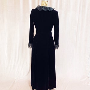 Pode incluir: Um vestido maxi de veludo preto com colarinho e punhos de renda. O vestido tem um corpete justo e uma saia fluida.
