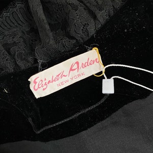 Pode incluir: Um tecido de veludo preto com uma guarni&ccedil;&atilde;o de renda preta e uma etiqueta branca que diz "Elizabeth Arden NEW YORK".