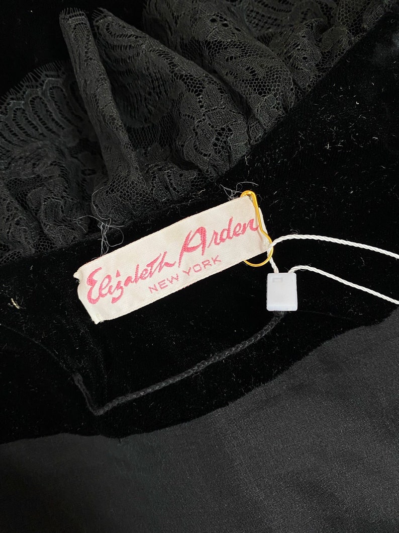 Pode incluir: Um tecido de veludo preto com uma guarni&ccedil;&atilde;o de renda preta e uma etiqueta branca que diz "Elizabeth Arden NEW YORK".