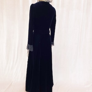 Pode incluir: Um vestido longo de veludo preto com colarinho e punhos de renda. O vestido tem um corpete justo e uma saia fluida.