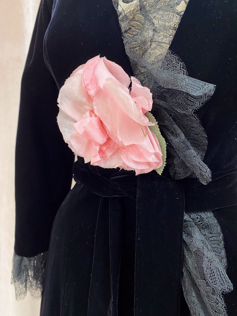 Pode incluir: Um roup&atilde;o de veludo preto com uma flor rosa e guarni&ccedil;&atilde;o de renda preta.