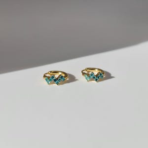 The Lumen 18k Gold Plated Stainless Steel Clustered Crystal Huggie Hoop Earrings in Aquamarine Blue Cubic Zirconia.