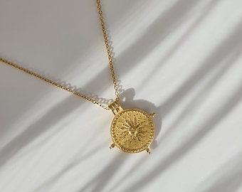 May include: A gold necklace with a circular pendant. The pendant has a sunburst design with small dot details and four small decorative points. The chain is thin and delicate.